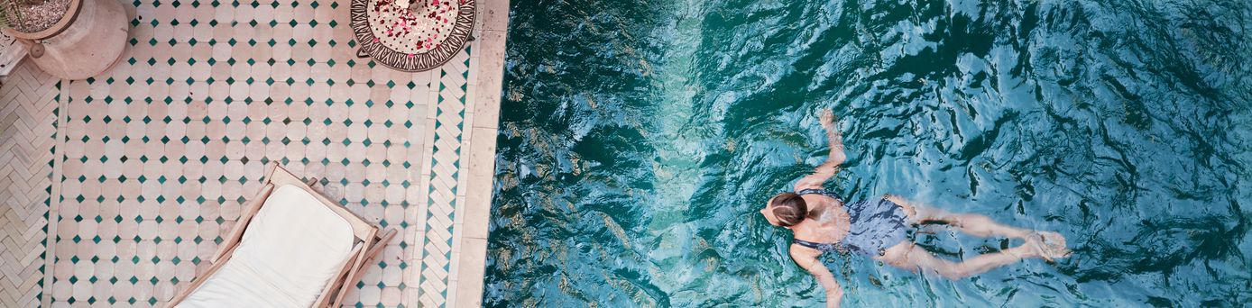 Frau schwimmt in einem Pool; Neben dem Pool, auf der Terrasse steht eine Liege
