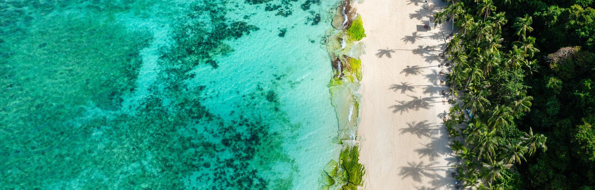 Ein Strand von oben, im Meer sieht man Riffe