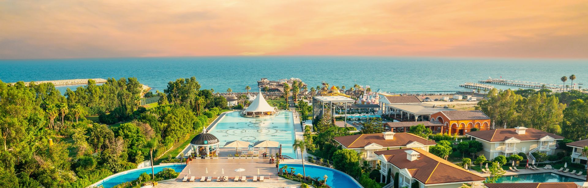 Zwei große Pools umgeben von Bäumen und mit Blick auf das Meer