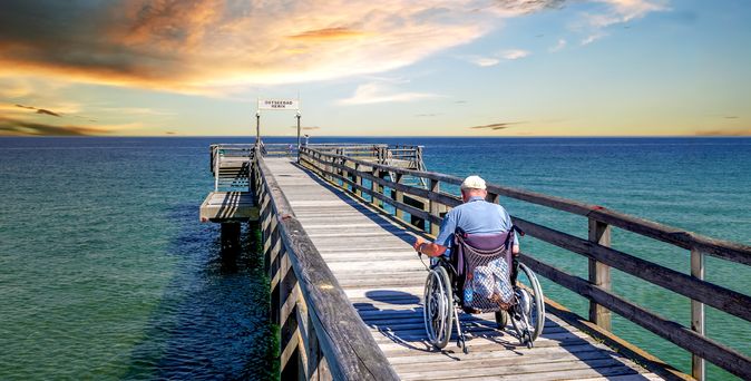 Mann im Rollstuhl auf einer Seebrücke am Meer
