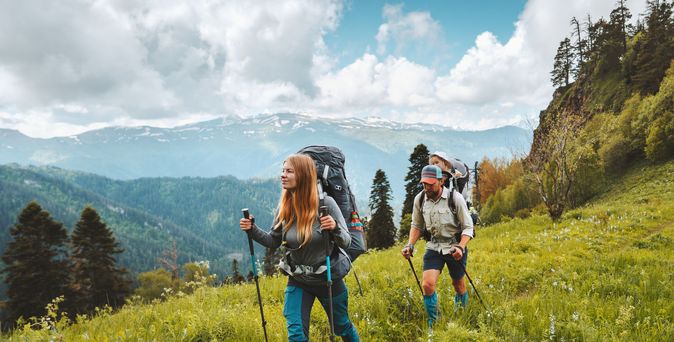 Zwei Personen wandern mit Nordic Walking Stöckern durch eine Wiese