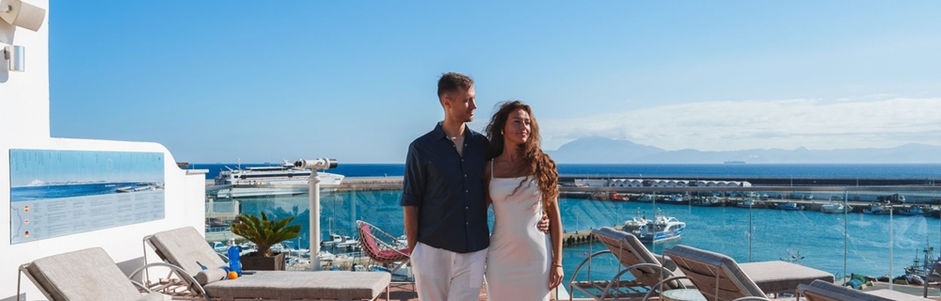 Ein Pärchen geht Arm in Arm über die Sonnenterasse eines Pools