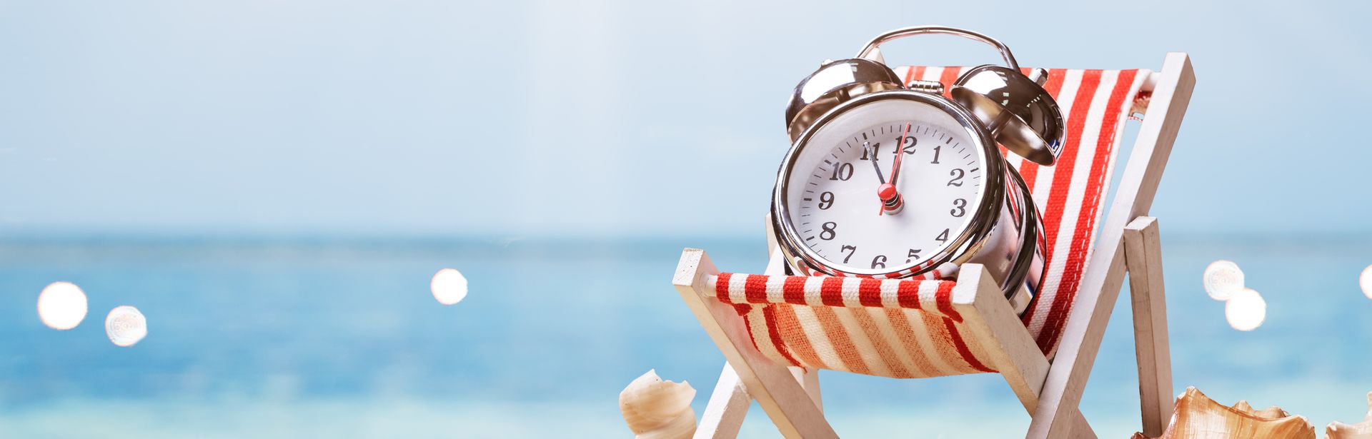 Ein Wecker liegt in einer Liege am Strand