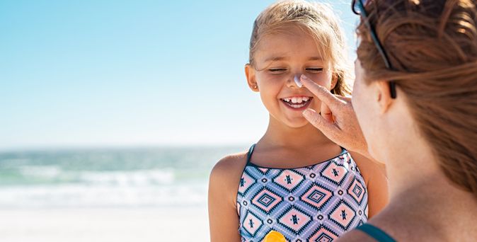 Mutter cremt ihre Tochter mit Sonnencreme im Gesicht ein