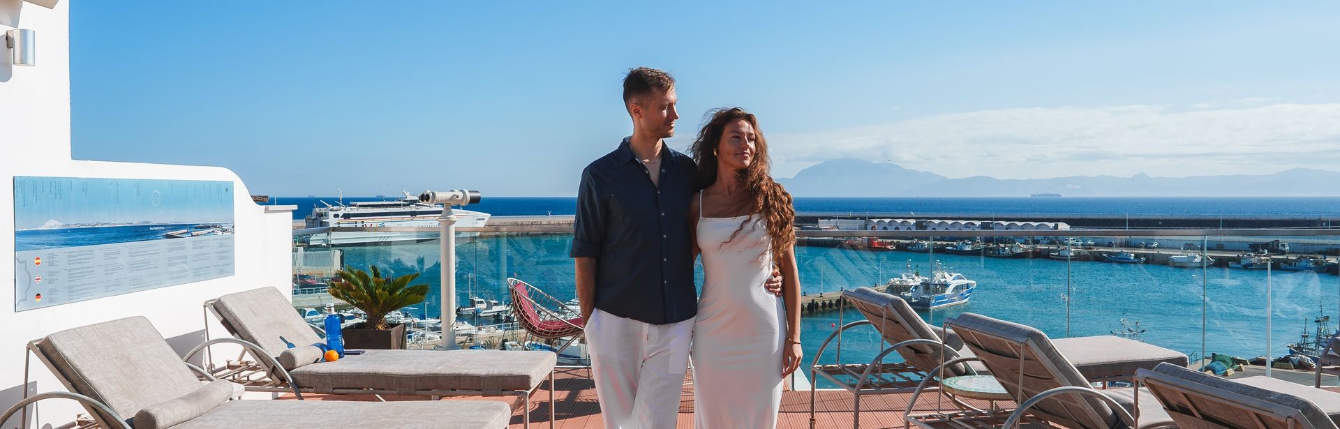 Pärchen geht Arm in Arm über die Sonnenterasse eines Pools