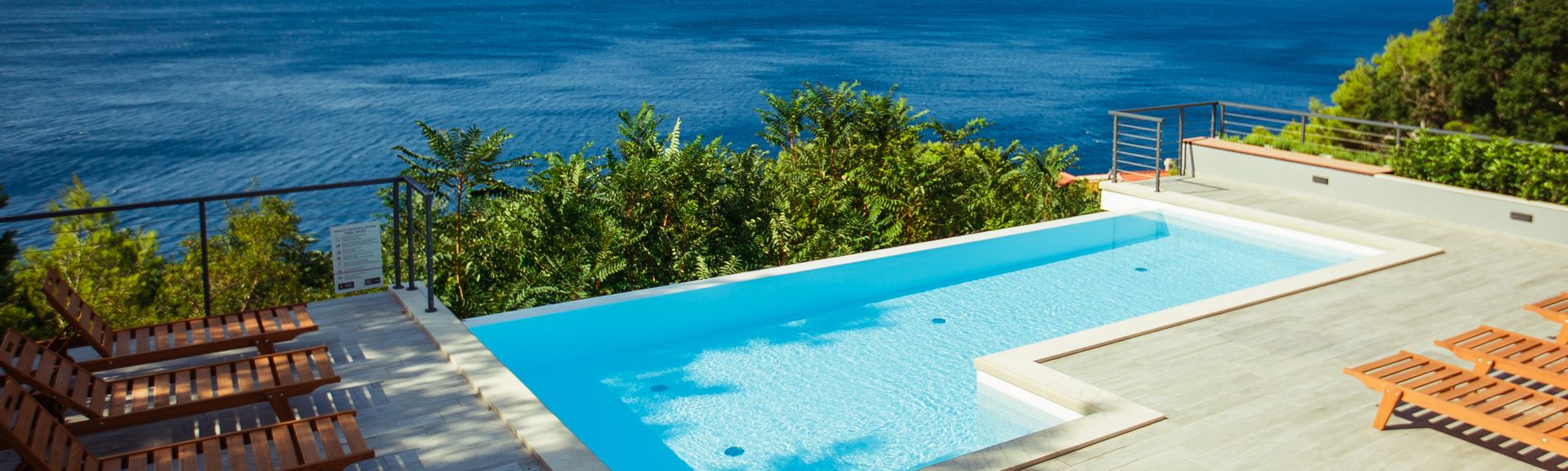 Ein Privatpool über dem Meer, um ihn herum einige Holzliegen und Bäume