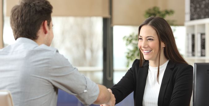 Eine Frau sitzt an einem Schreibtisch. Ihr gegenüber sitzt ein Mann und die beiden geben sich die Hand