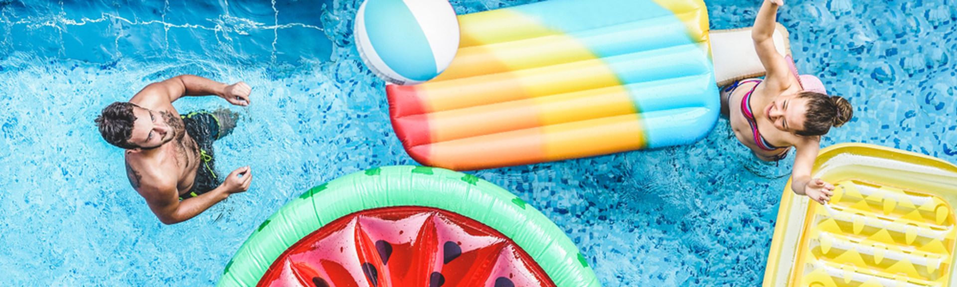 Ein Pool von oben, mehrere Personen und Pool Floaties in Frucht Formen
