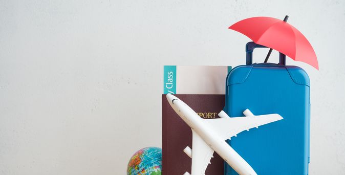 Ein Spielzeugkoffer, ein Spielzeugsonnenschirm, ein Spielzeugflugzeug, ein Reisepass und eine kleine Weltkugel stehen auf einem Tisch