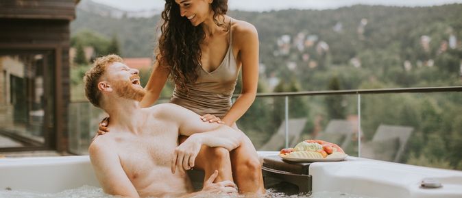 Ein Mann sitzt im Whirlpool und eine Frau sitzt hinter ihm auf dem Rand des Whirlpools