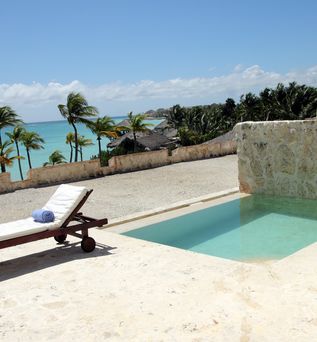 Eine höher gelegene Terrasse mit einem kleinen privaten Pool, einer Liege und Blick auf das Meer und Palmen