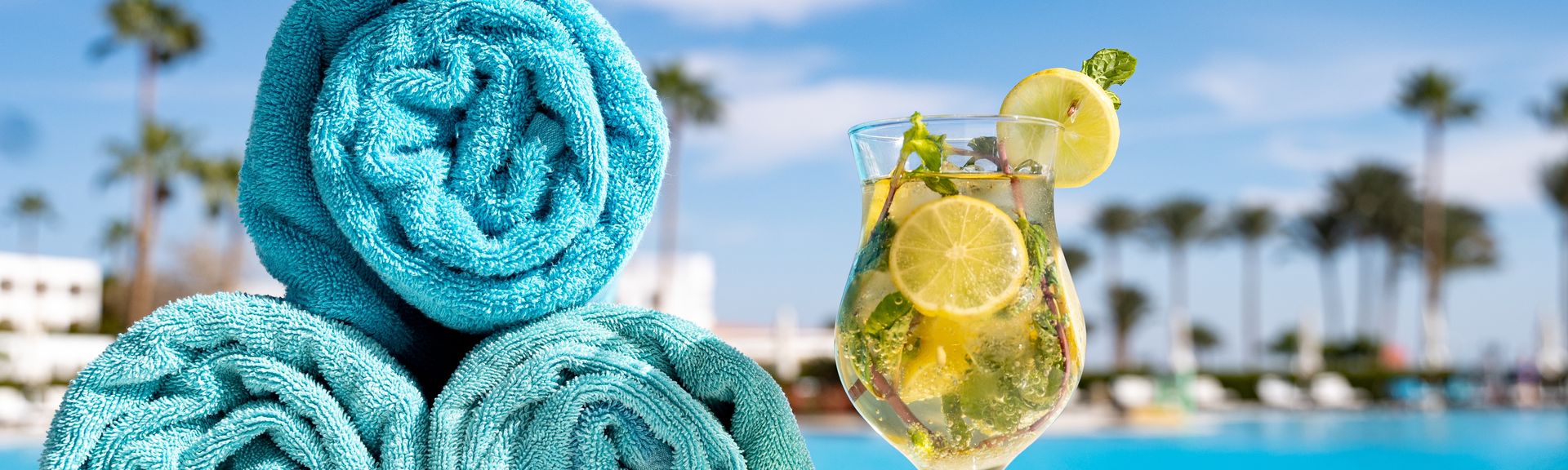 Handtücher und ein Getränk stehen am Pool mit Palmen im Hintergrund