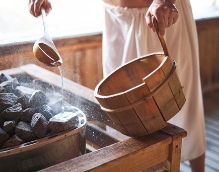 Ein Mann gießt Wasser auf heiße Steine in einer Sauna