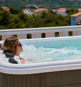 Eine Frau liegt entspannt im Whirlpool, im Hintergrund sind Häuser zu sehen