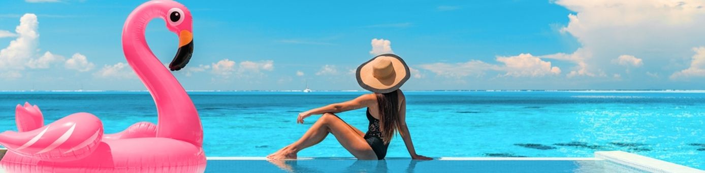 Frau sitzt am Rand eines Pools mit Meerblick, neben Ihr ein aufblasbarer Flamingo
