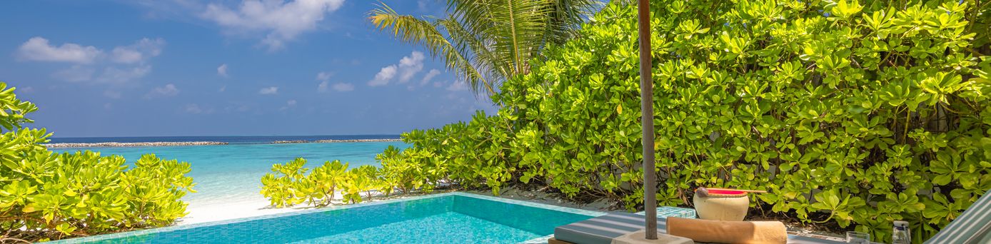 Zwei Liegen unter einem Sonnenschirm, vor einem kleinen Pool