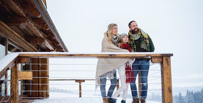 Familie steht in Winterklamotten auf der Terrasse eines Balkons während Schnee liegt