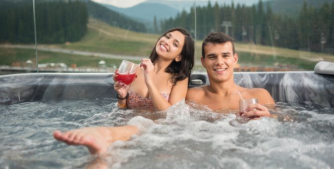 Ein Paar im Whirlpool. Die Frau trinkt ein rotes Getränk und lässt ihren Fuß aus dem Wasser schauen