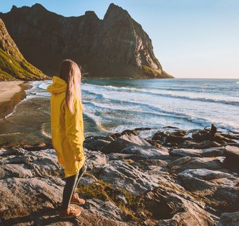 Eine Frau in einer gelben Regenjacke schaut auf das Meer