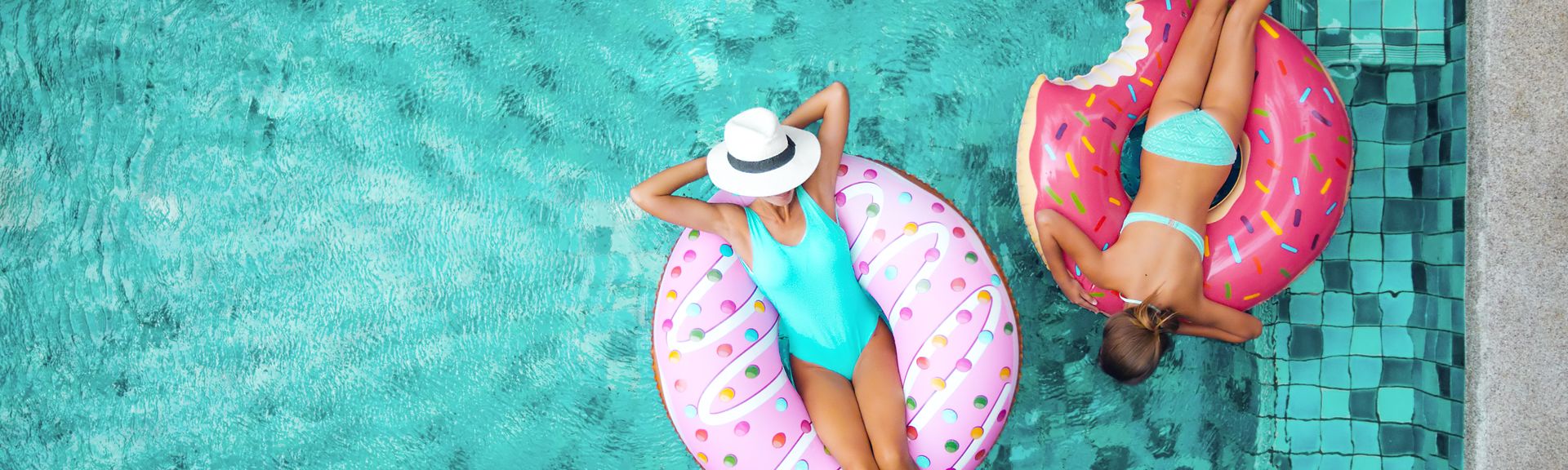 Zwei Frauen liegen in Donut Pool Floaties im Pool