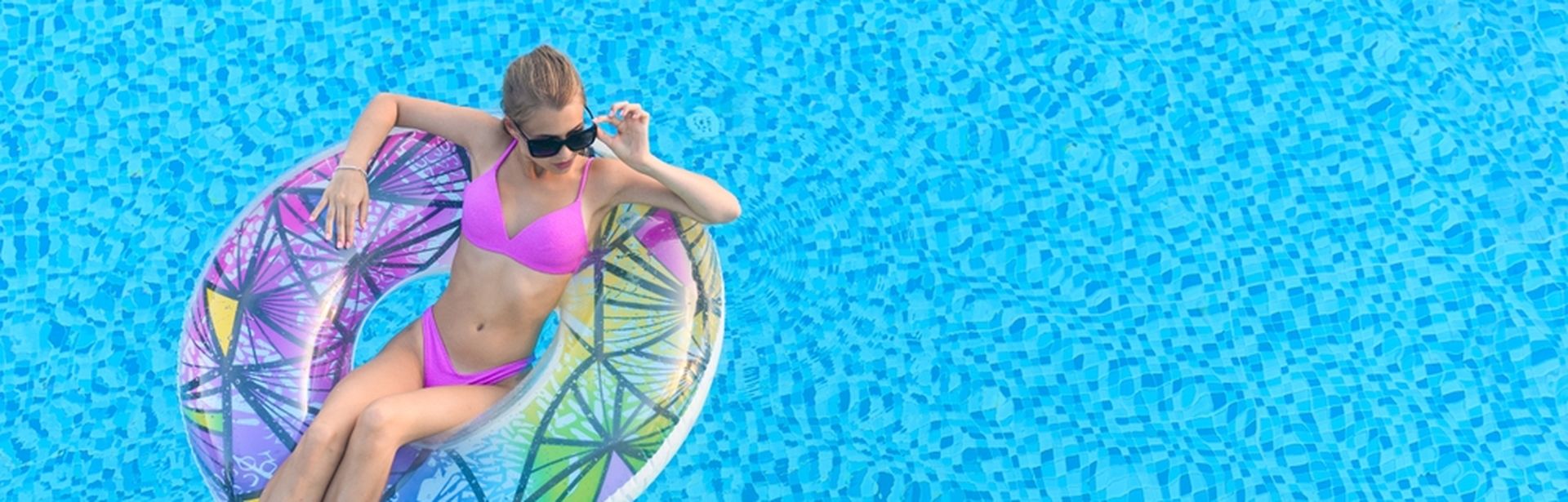 Eine Frau in einem pinken Bikini sitzt in einem Pool in einem bunten Poolfloatie