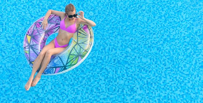 Eine Frau in einem pinken Bikini sitzt in einem Pool in einem bunten Poolfloatie