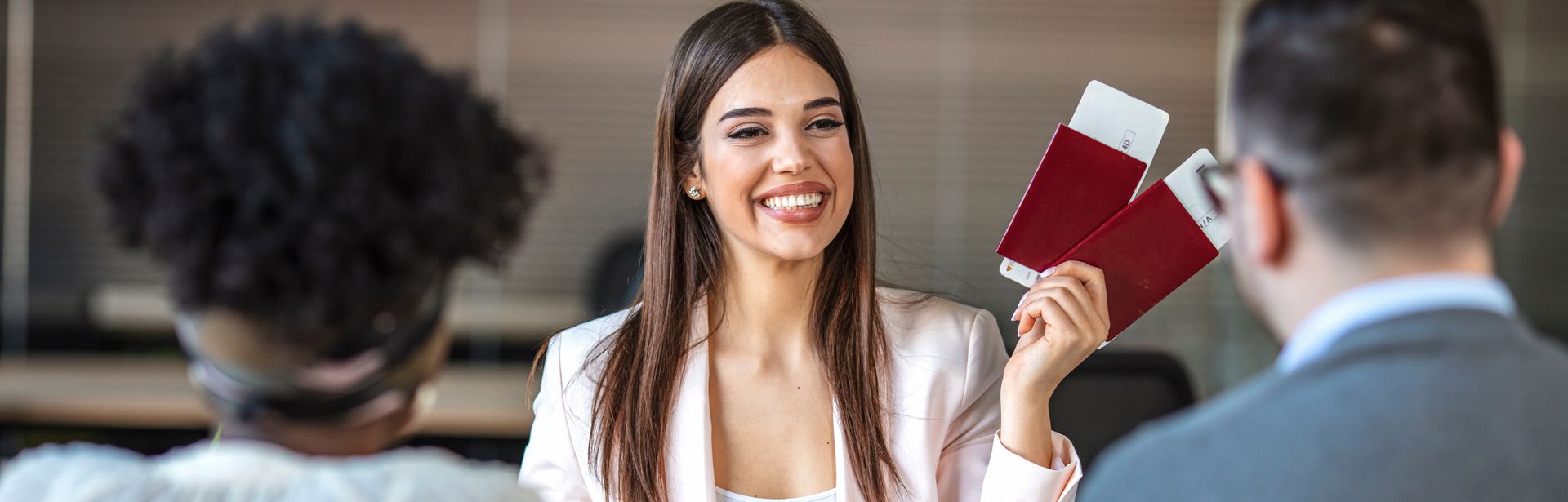 Eine lächelnde Reiseberaterin hält Ihren Kunden zwei Reisepässe mit Flugtickets hin