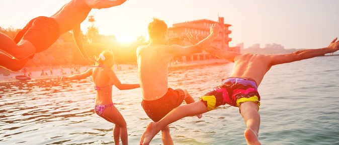 Vier Personen springen bei Sonnenuntergang ins Meer