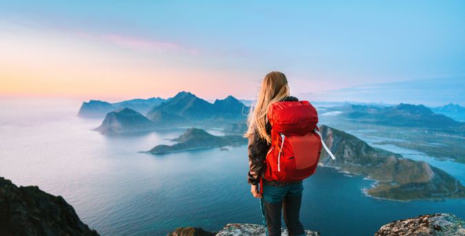 Eine Frau von hinten, Sie trägt einen großen Rucksack und schaut von einem Berg aus den Sonnenaufgang an