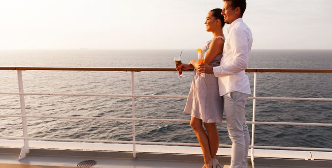 Ein Paar steht auf einem Kreuzfahrtschiff an der Reling und schaut aufs Meer