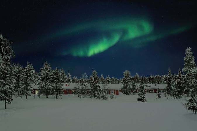 Polarlichter über einer Hütte im schneebedeckten Wald