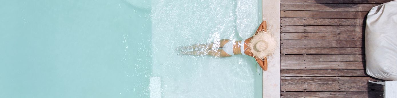 Eine Frau mit weißem Sonnenhut lehnt am Rand eines eleganten Pools