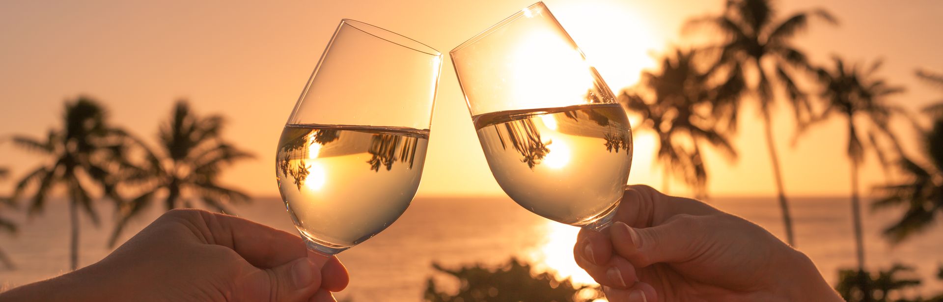 Zwei Hände stoßen am Strand mit Weingläsern an 