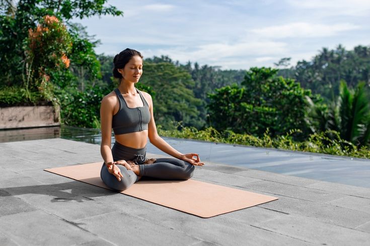 Eine Frau meditiert im Schneidersitz auf einer Yogamatte