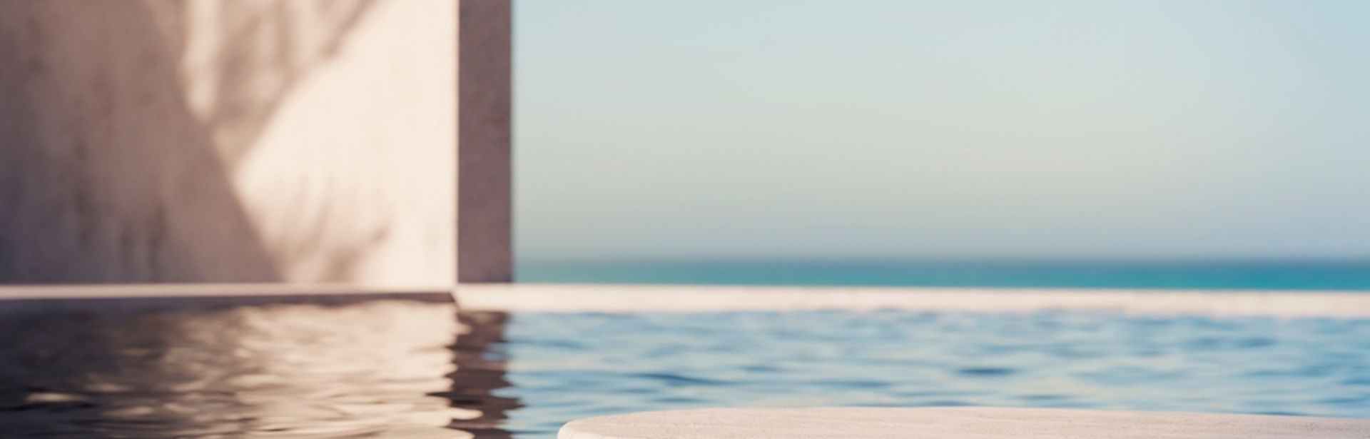 Eine Pooloberfläche auf der sich die Wand daneben spiegelt, im Hintergrund blauer Himmel