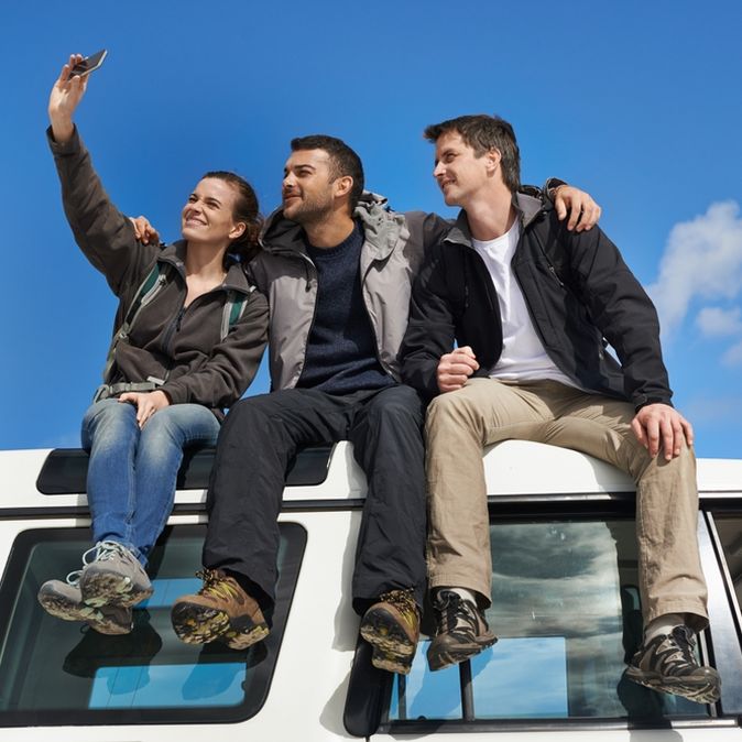 Drei Personen sitzen auf einem weißen Jeep und machen lächelnd ein Selfie